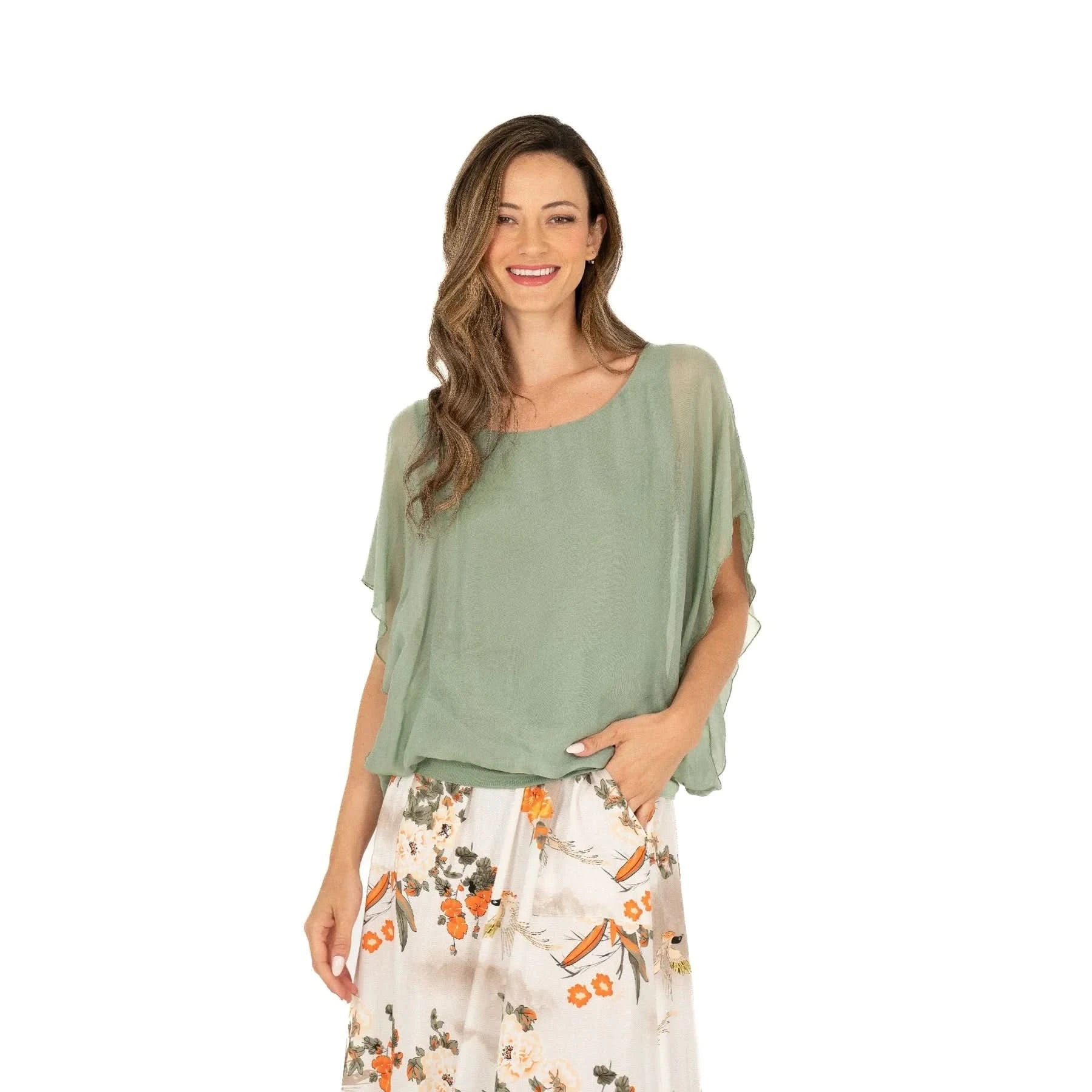 A woman with long hair is wearing a comfortable and stylish Ladies Woven Top by M Made In Italy in light green and a floral skirt, standing sideways against a plain white background.