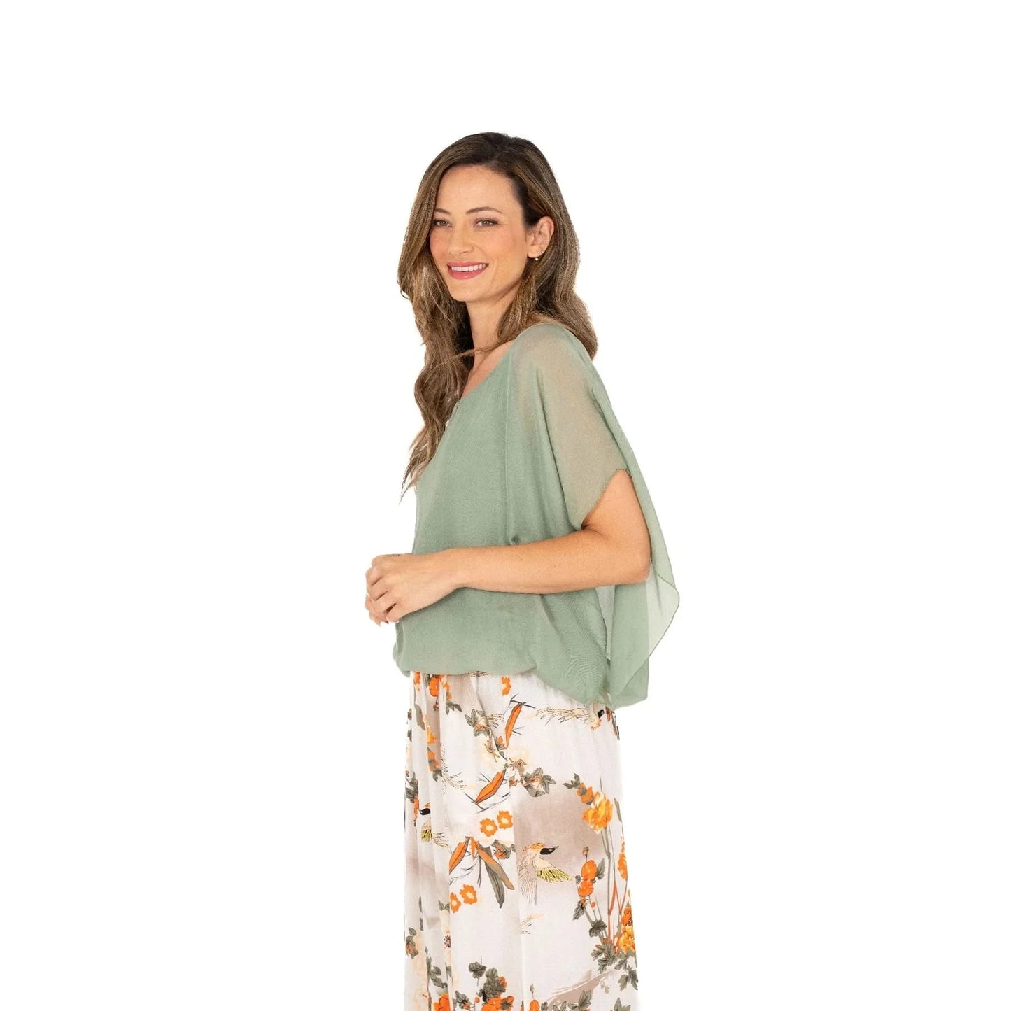 A woman with long hair is wearing a comfortable and stylish Ladies Woven Top by M Made In Italy in light green and a floral skirt, standing sideways against a plain white background.