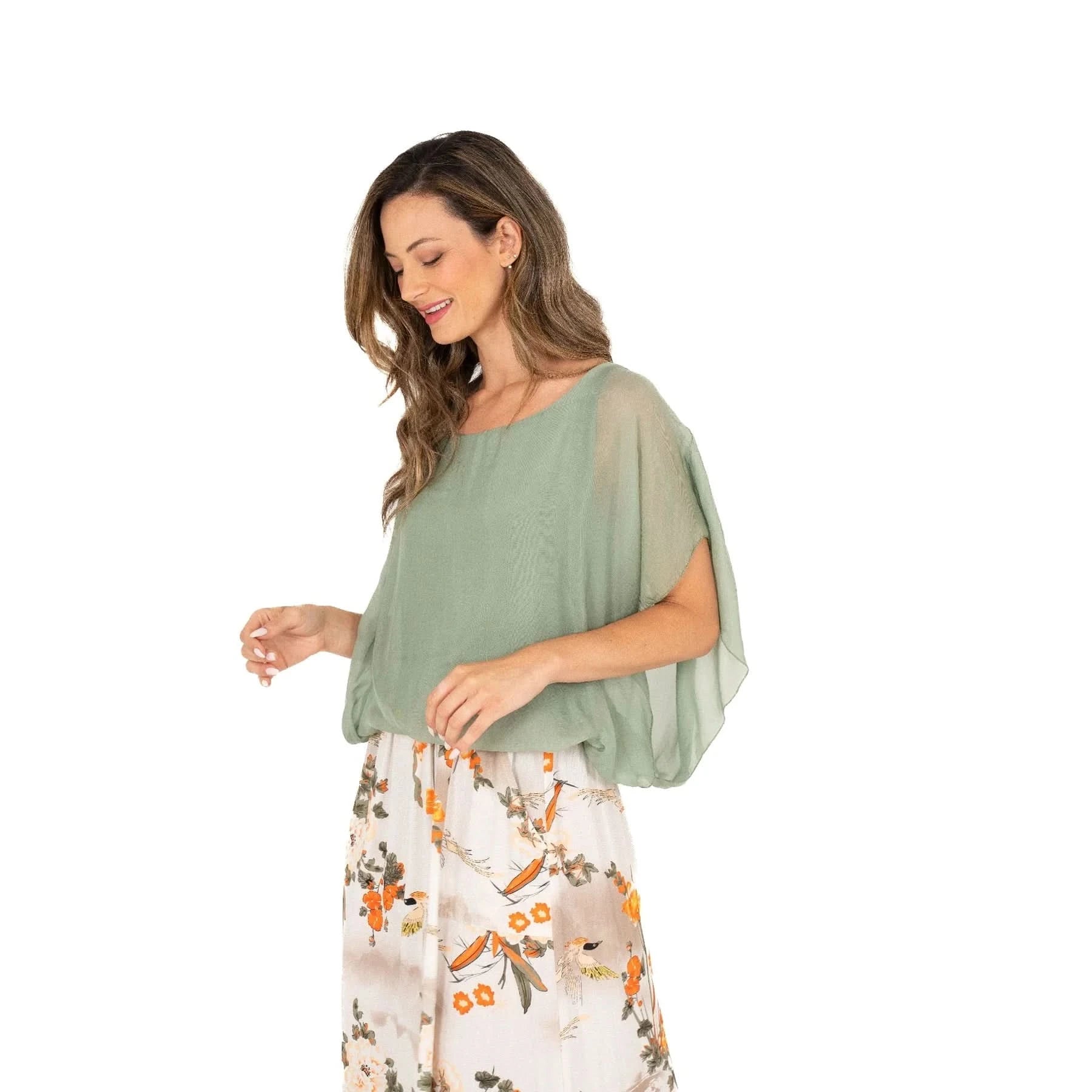 A woman with long hair is wearing a comfortable and stylish Ladies Woven Top by M Made In Italy in light green and a floral skirt, standing sideways against a plain white background.