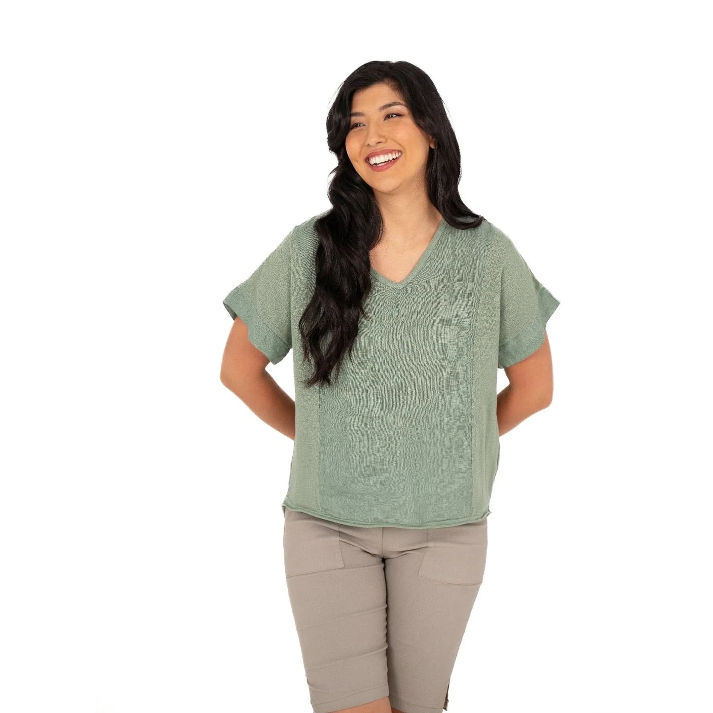A person smiles while wearing the M Made In Italy V Neck Woven Top in green, paired with beige shorts against a white background.