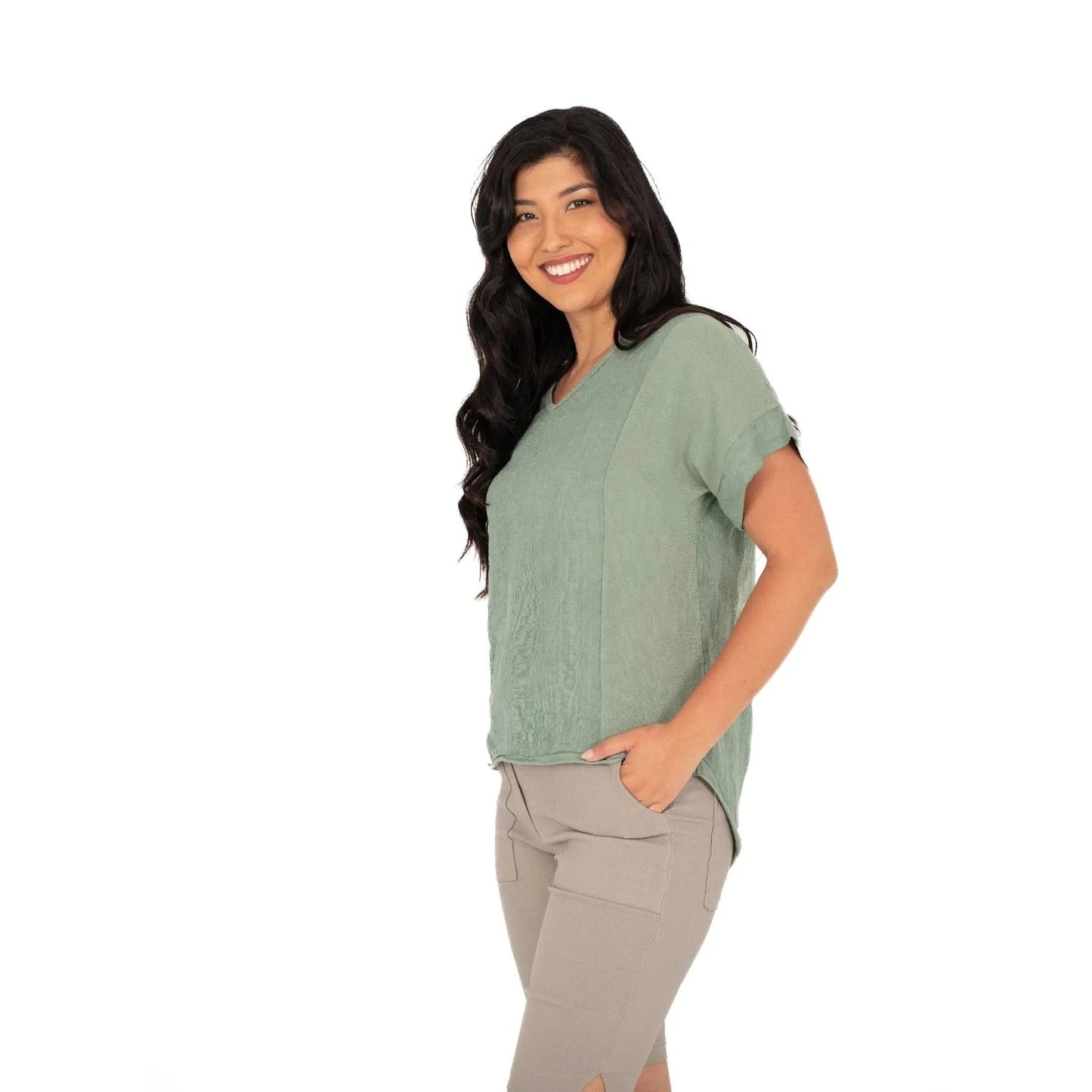 A person smiles while wearing the M Made In Italy V Neck Woven Top in green, paired with beige shorts against a white background.