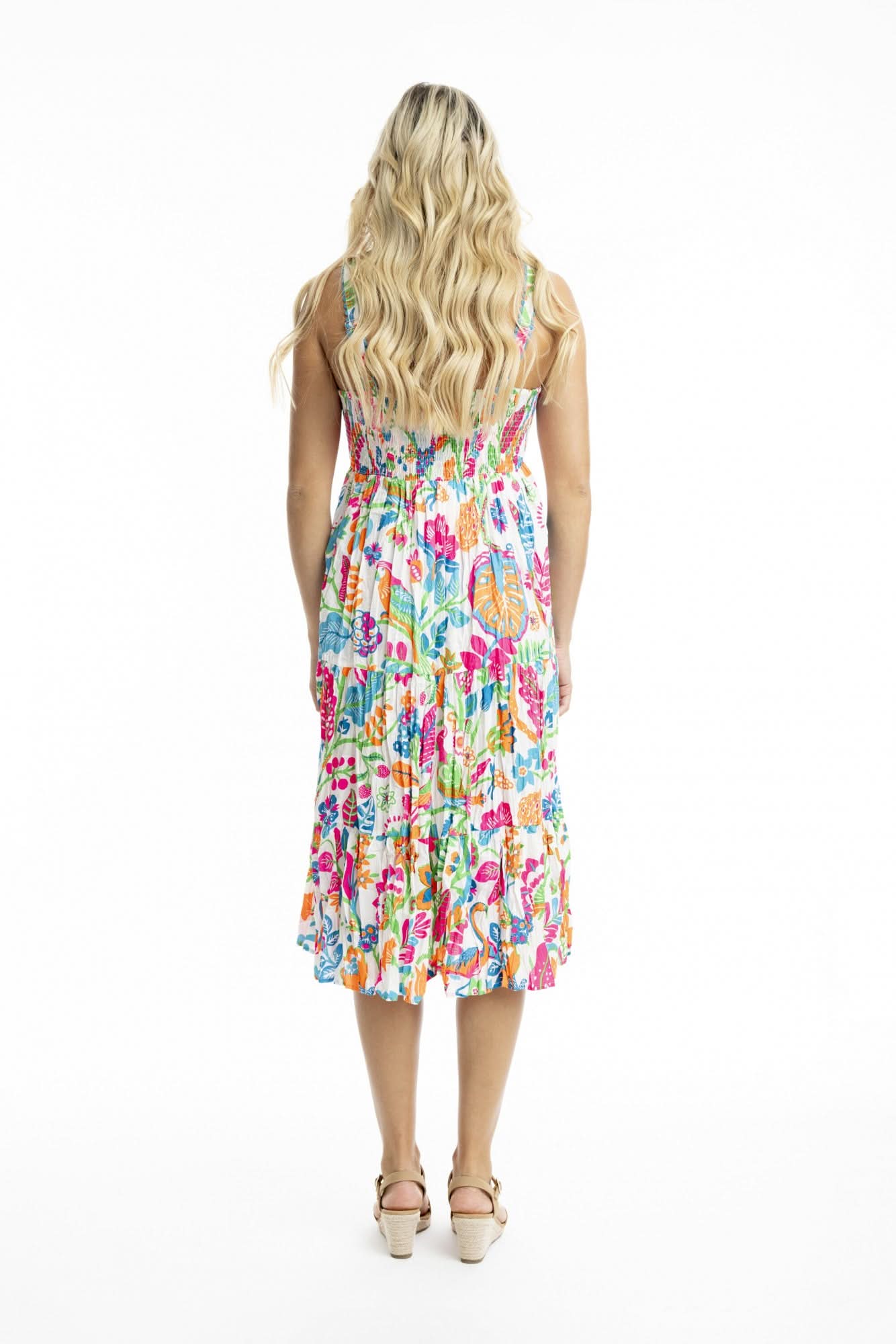 Woman facing forward, wearing the Orientique Madurai Strappy Dress—a colorful, floral sleeveless summer dress—and beige sandals against a plain white background.