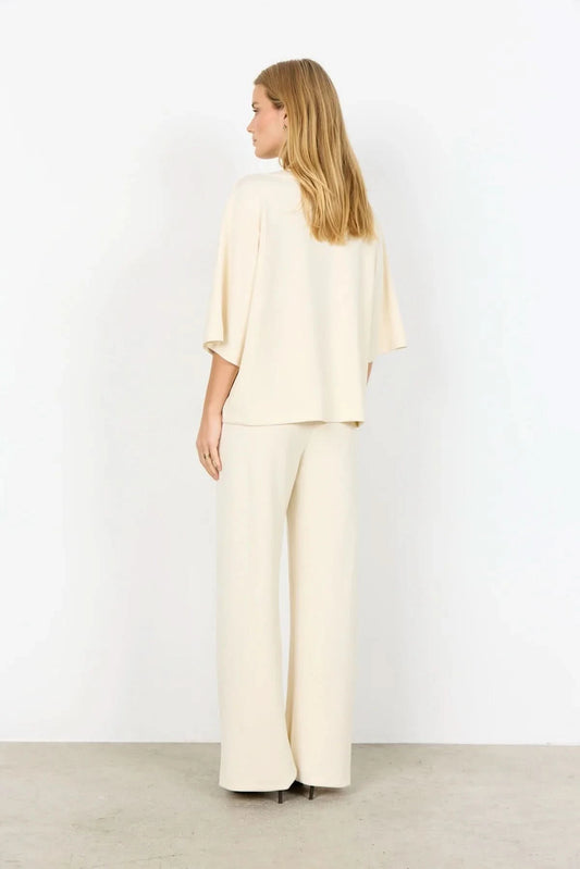A woman with long blonde hair wears the Soya Concepts Banu Top, its elegant silhouette highlighted as she stands against a plain white background.