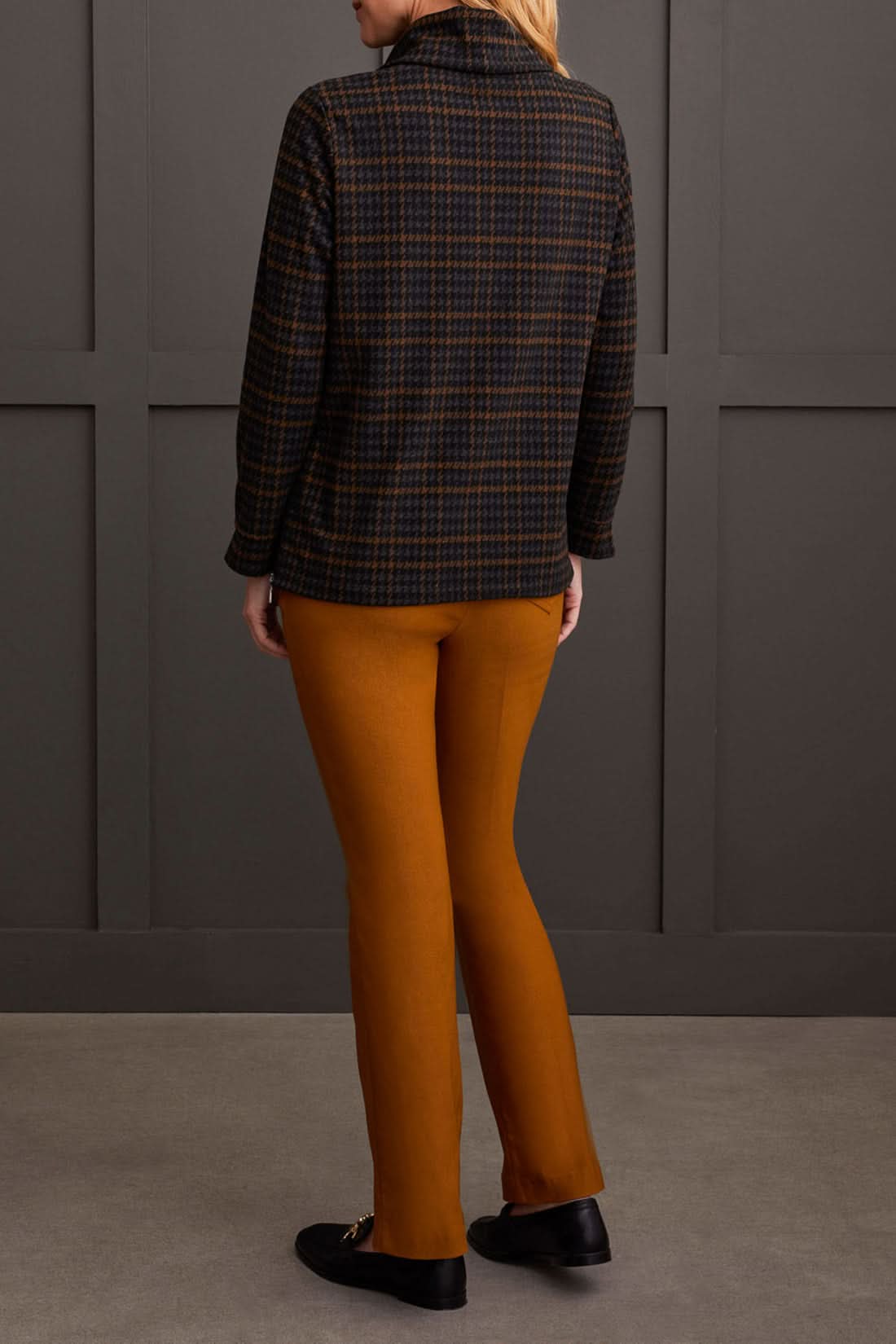 The person is wearing a chic cowl neck top with a side zipper by Tribal, paired with brown pants, standing comfortably in front of a gray paneled wall.