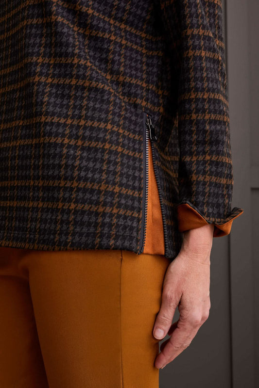 The person is wearing a chic cowl neck top with a side zipper by Tribal, paired with brown pants, standing comfortably in front of a gray paneled wall.