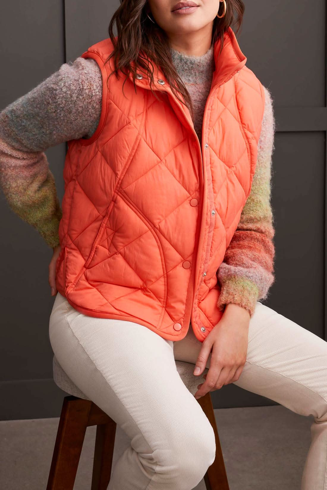 Person wearing a cozy black A Line Puffer Vest from Tribal over a red sweater with plaid pants, making a fashion statement while standing in front of a gray background.