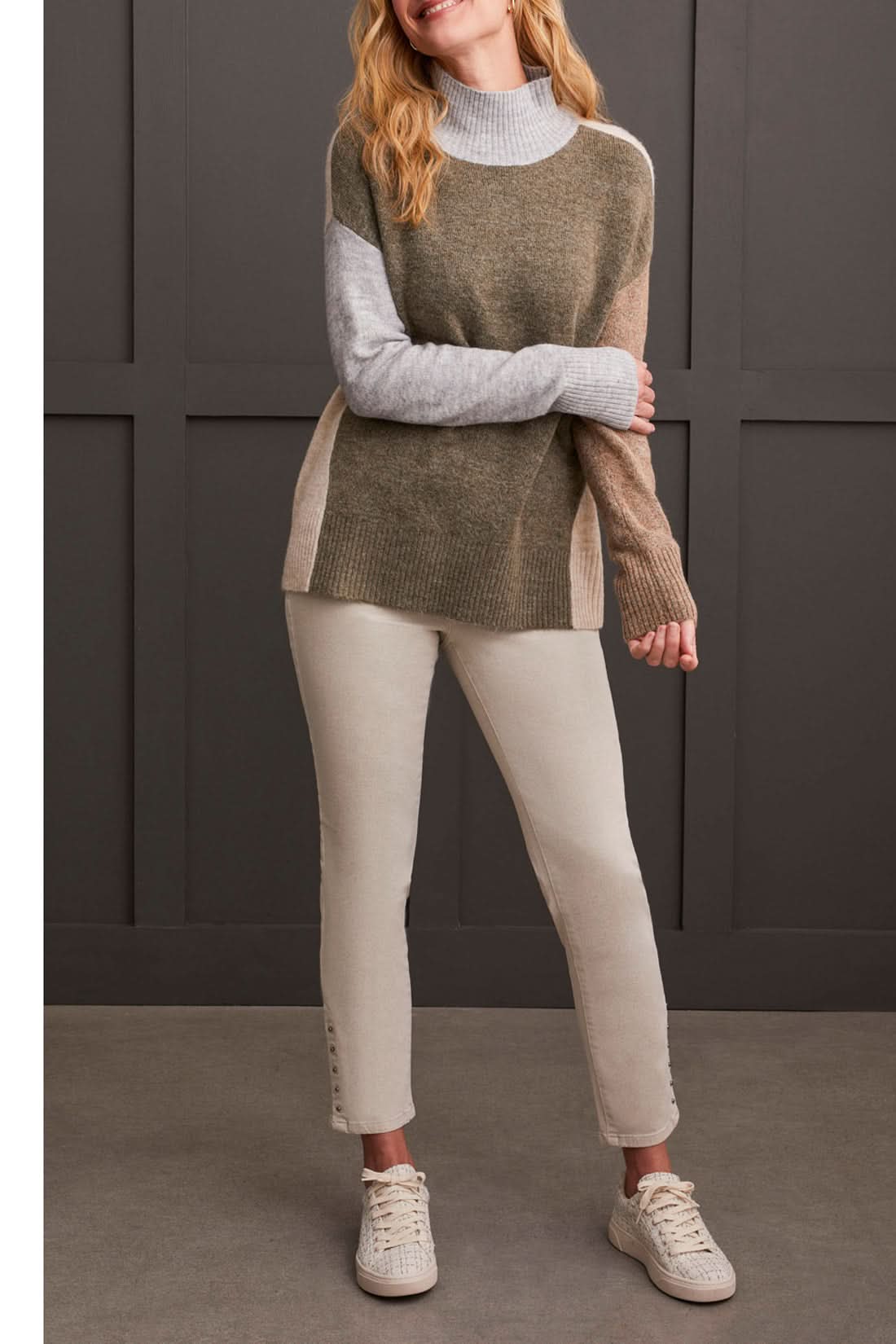 A person wearing the Mock Neck Colorblock Sweater by Tribal, featuring cozy gray, brown, and beige stripes, smiles while holding the collar near their face—truly a fall staple.