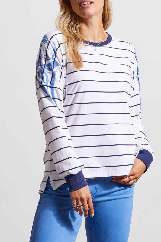 Woman in a stylish, striped Tribal Long Sleeve Drop Shoulder Crew Neck shirt and blue pants posing with one hand on her hip.