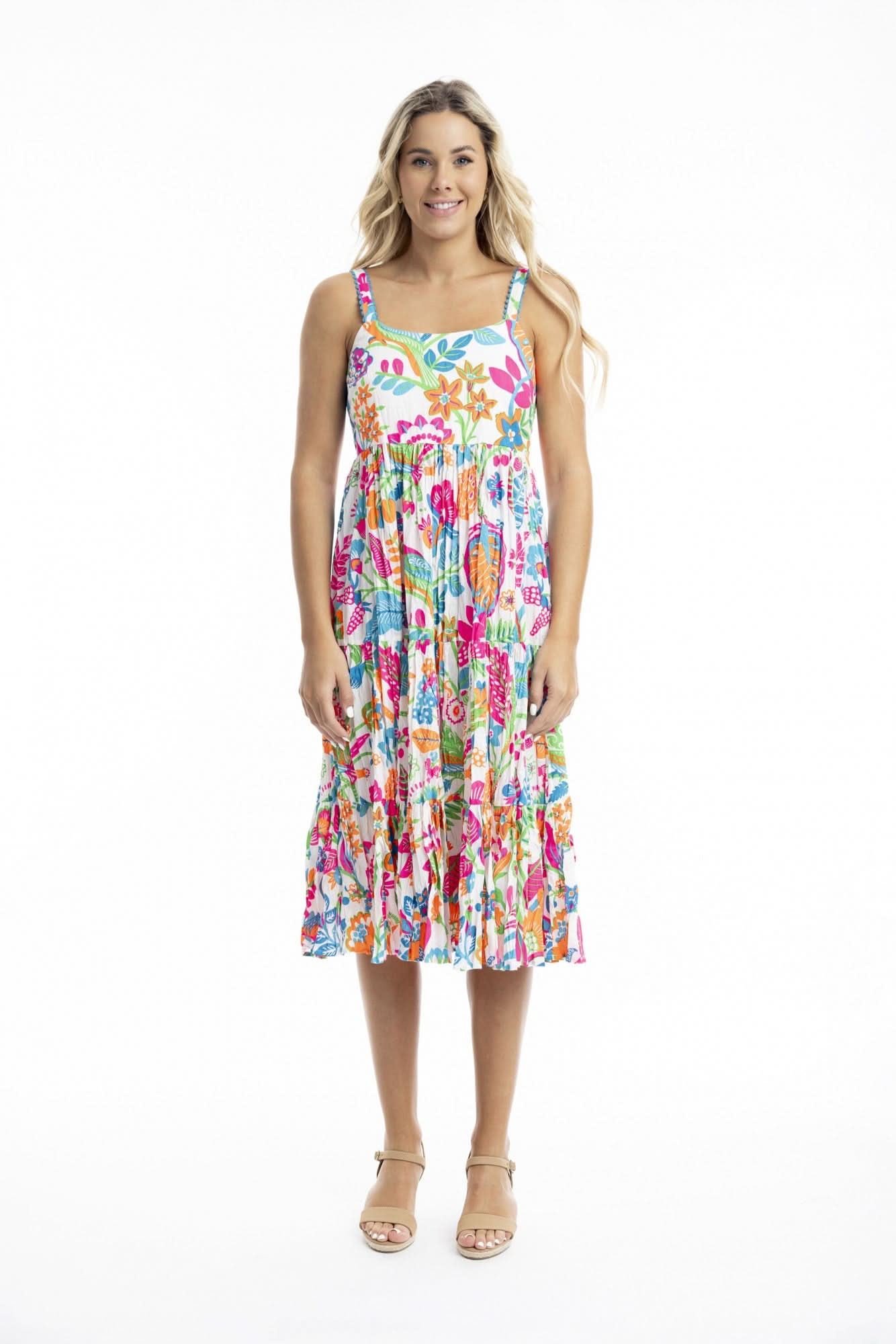 Woman facing forward, wearing the Orientique Madurai Strappy Dress—a colorful, floral sleeveless summer dress—and beige sandals against a plain white background.