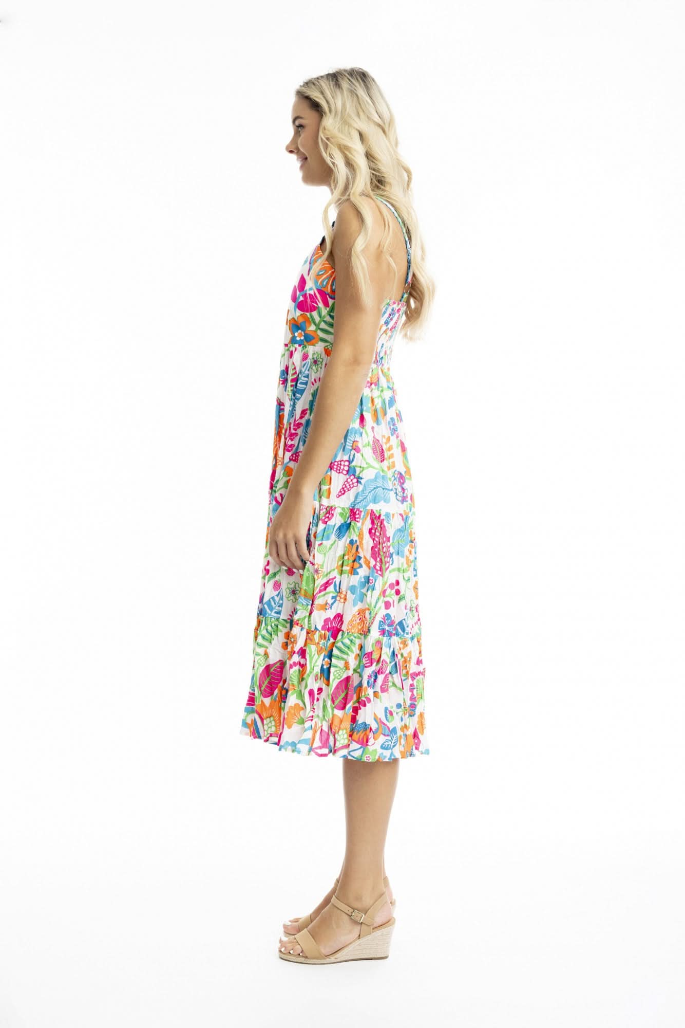 Woman facing forward, wearing the Orientique Madurai Strappy Dress—a colorful, floral sleeveless summer dress—and beige sandals against a plain white background.