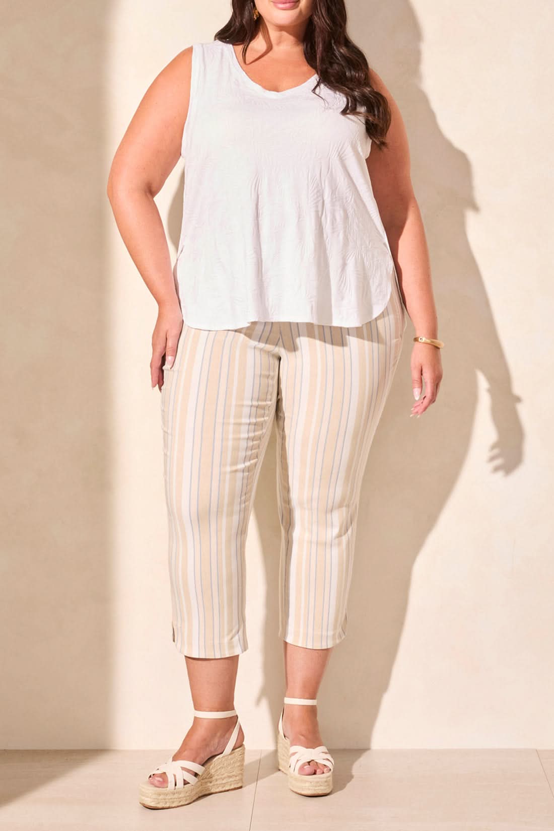 A woman wearing a Tribal TEXTURED V-NECK TANK WITH SIDE SLITS in an olive-green pattern and light-colored pants stands against a white background.