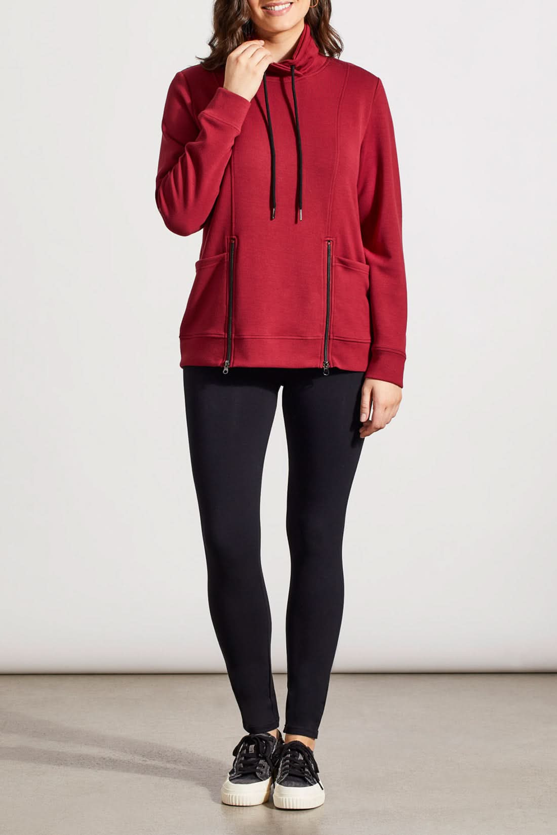 Individual dressed in a red Funnel Neck Top with Pockets by Tribal, featuring drawstrings and crafted from high-quality material, complemented by black pants.