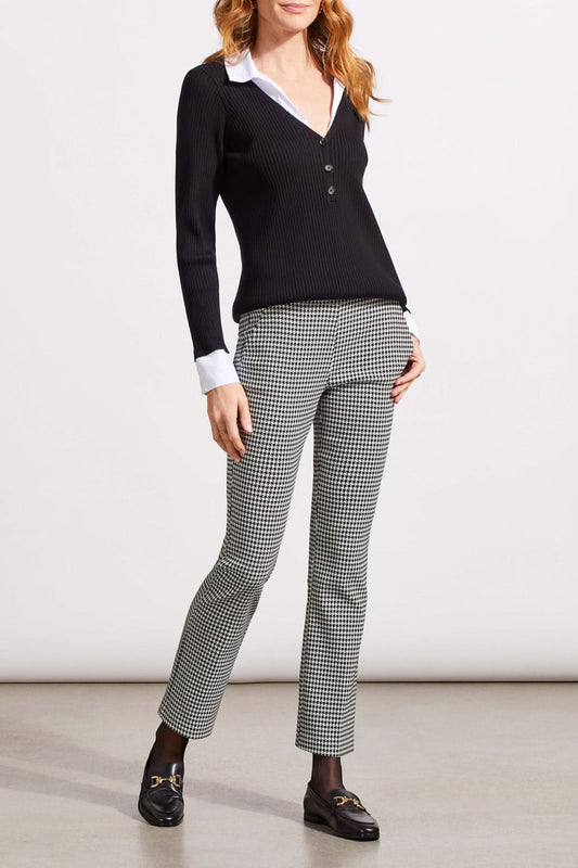 Close-up of a person showcasing the Tribal Houndstooth Pull on Pant, blending comfort and style with its classic houndstooth pattern. They're paired with a black sweater over a white cuffed shirt, revealing part of the torso and one hand.