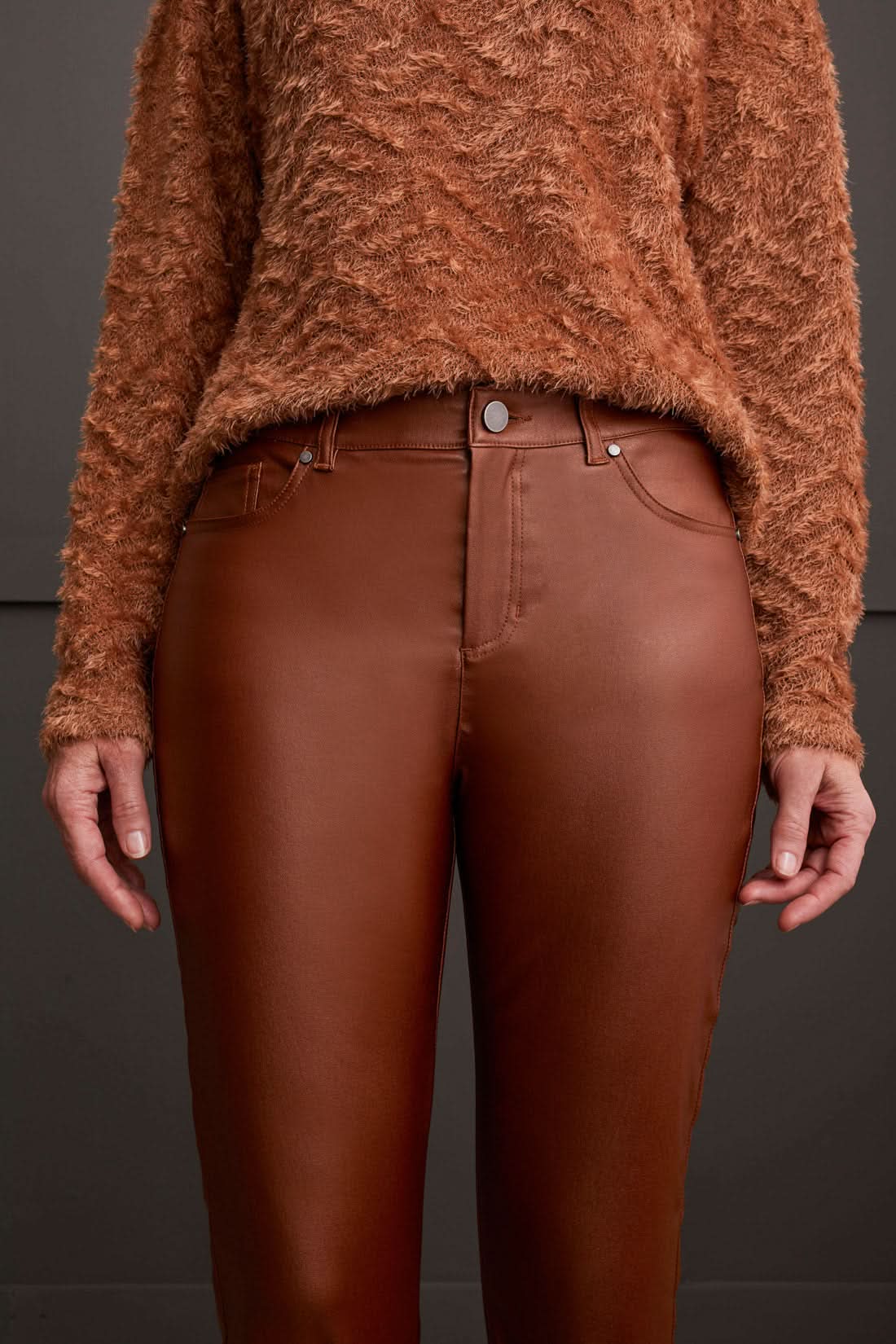 A person stands wearing a textured brown sweater, stylish Tribal Front Fly 5 Pocket Pant, and brown shoes against a gray paneled wall.