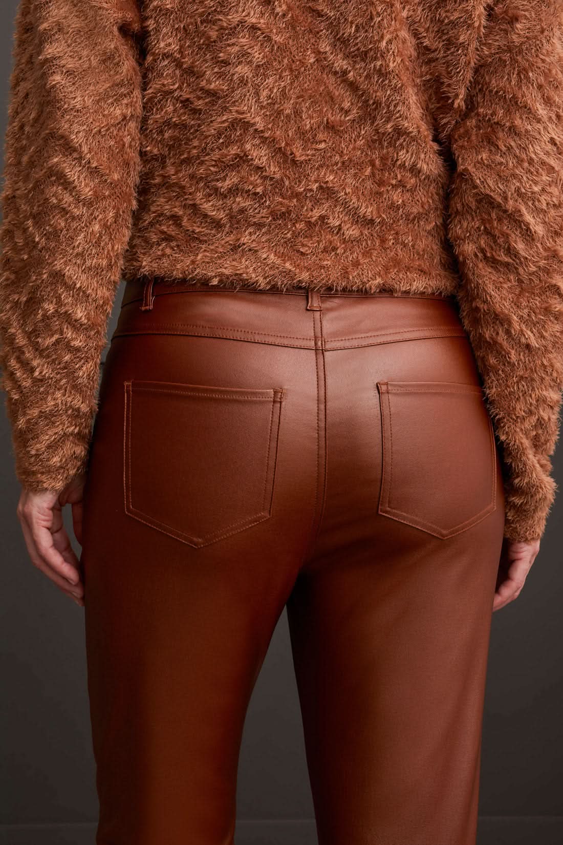 A person stands wearing a textured brown sweater, stylish Tribal Front Fly 5 Pocket Pant, and brown shoes against a gray paneled wall.