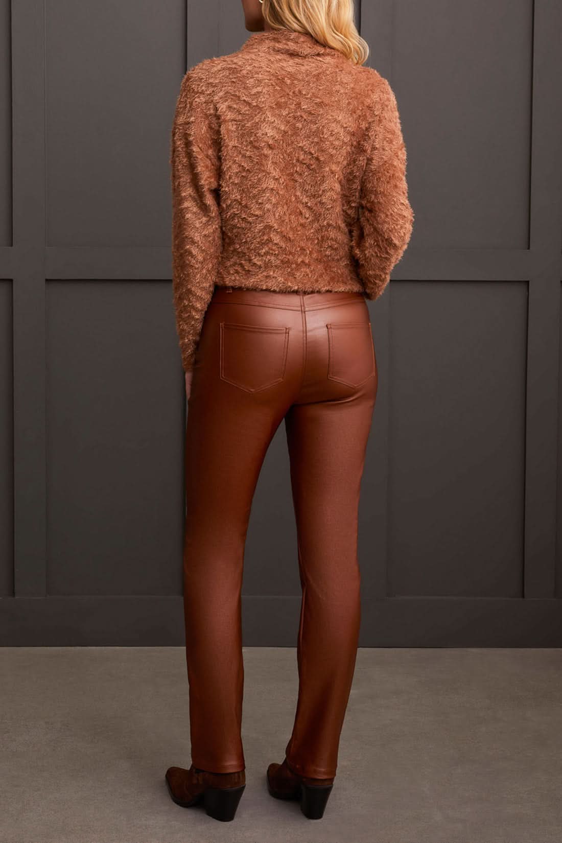 A person stands wearing a textured brown sweater, stylish Tribal Front Fly 5 Pocket Pant, and brown shoes against a gray paneled wall.