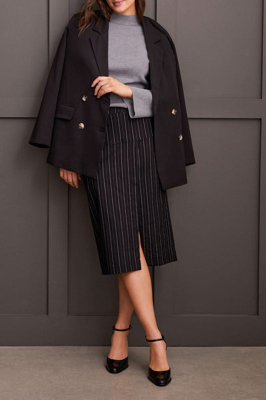 A person wearing a grey long-sleeve top and a black pinstripe pencil skirt with a slit, standing confidently with one hand on their hip, showcasing effortless style. This Striped Pull on Skirt by Tribal is a versatile addition to any wardrobe.