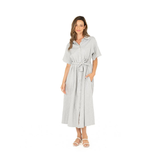Against a white background, a woman wears the Button Up Short Sleeve Dress with Front Tie by M Made In Italy. Paired with white sandals, her stylish and practical striped dress exudes effortless charm and modern elegance.