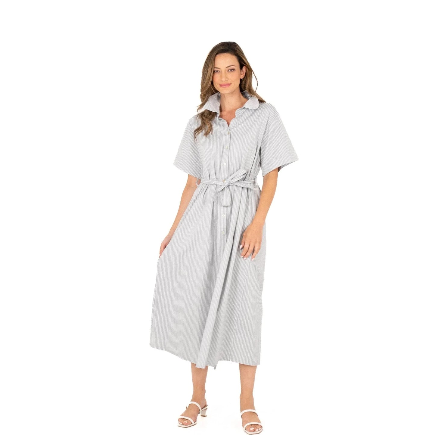 Against a white background, a woman wears the Button Up Short Sleeve Dress with Front Tie by M Made In Italy. Paired with white sandals, her stylish and practical striped dress exudes effortless charm and modern elegance.