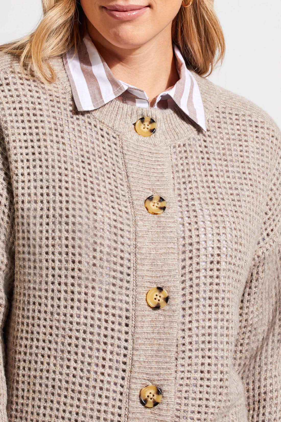 A person wearing a Crew Neck Sweater Cardigan by Tribal in beige, paired with a striped shirt, blue jeans, and brown boots stands against a plain background.