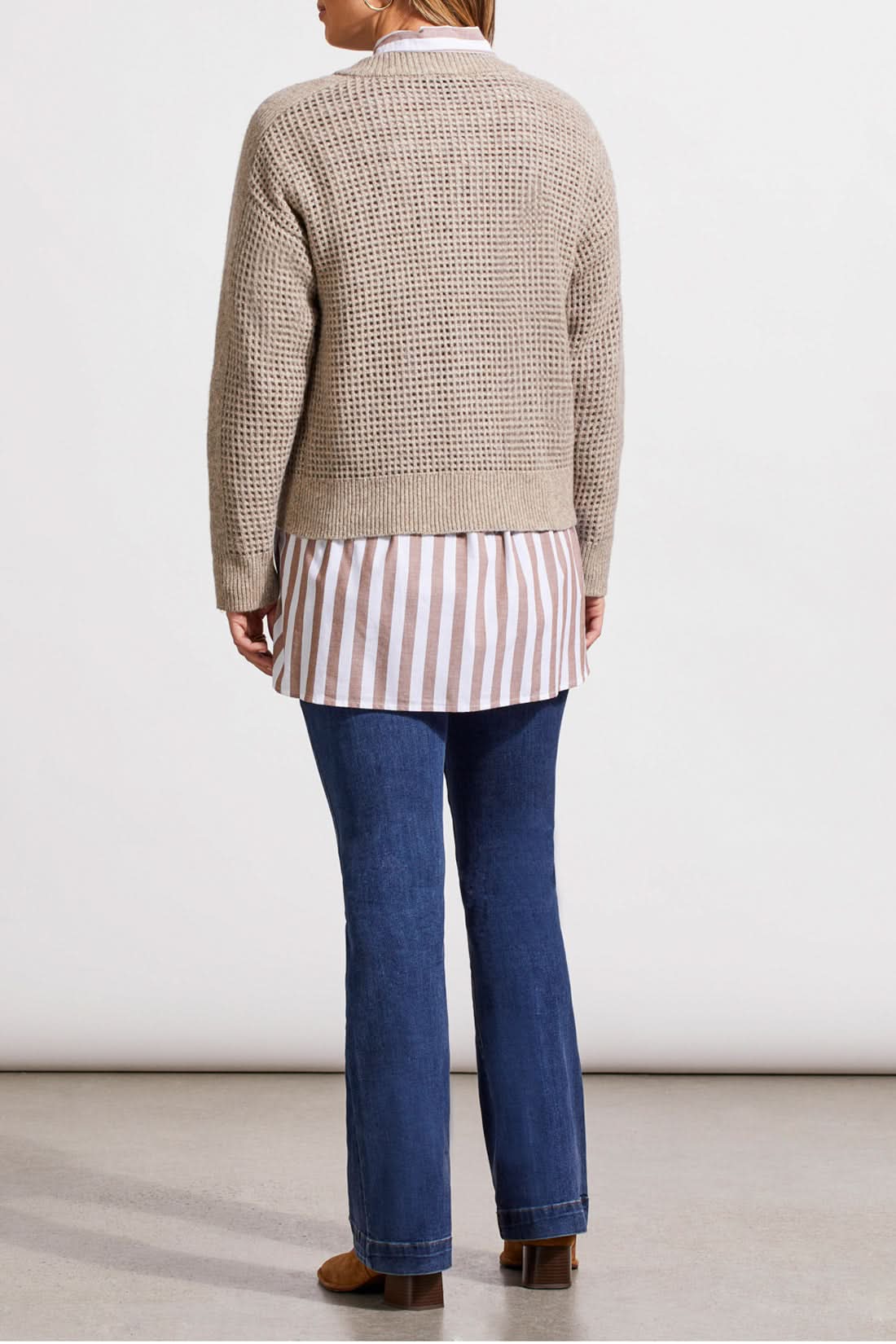 A person wearing a Crew Neck Sweater Cardigan by Tribal in beige, paired with a striped shirt, blue jeans, and brown boots stands against a plain background.