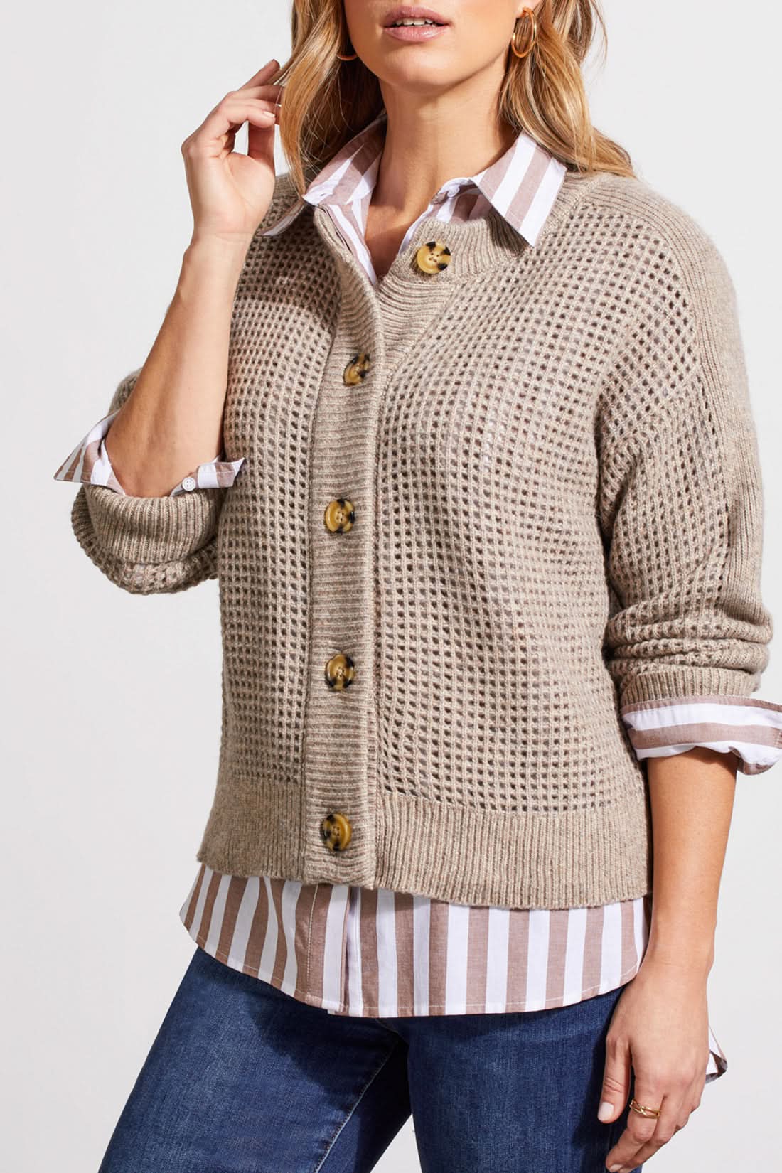 A person wearing a Crew Neck Sweater Cardigan by Tribal in beige, paired with a striped shirt, blue jeans, and brown boots stands against a plain background.