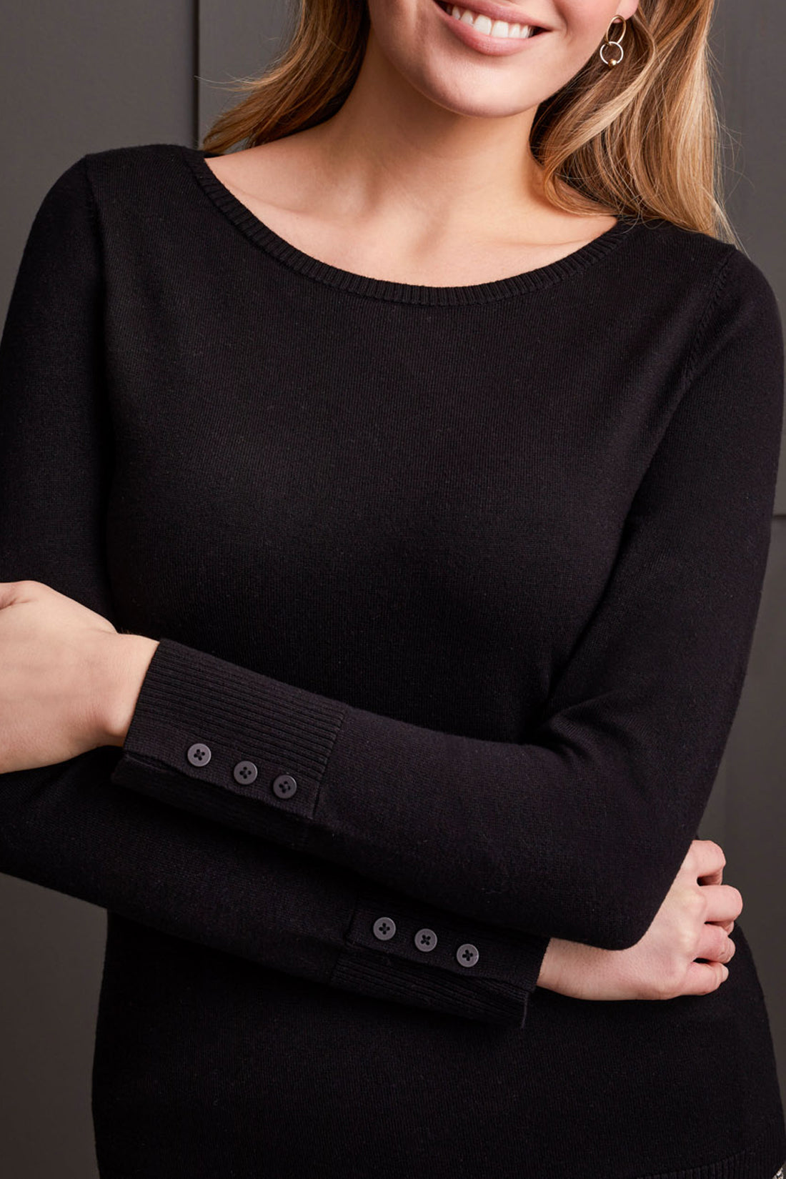 A person wearing a Tribal Boat Neck Sweater with long sleeves and button sleeve details, standing in front of a dark background.