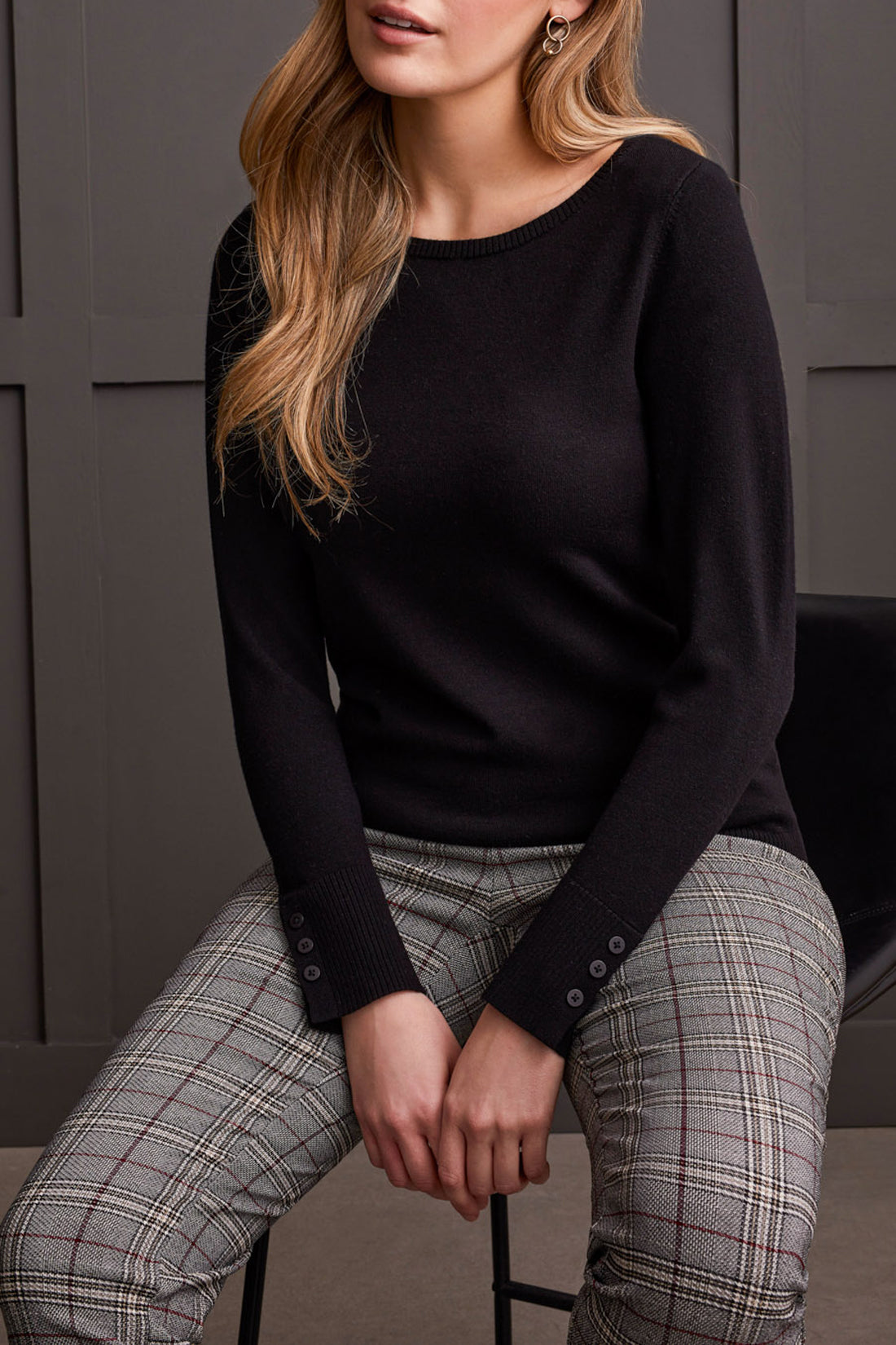 A person wearing a Tribal Boat Neck Sweater with long sleeves and button sleeve details, standing in front of a dark background.