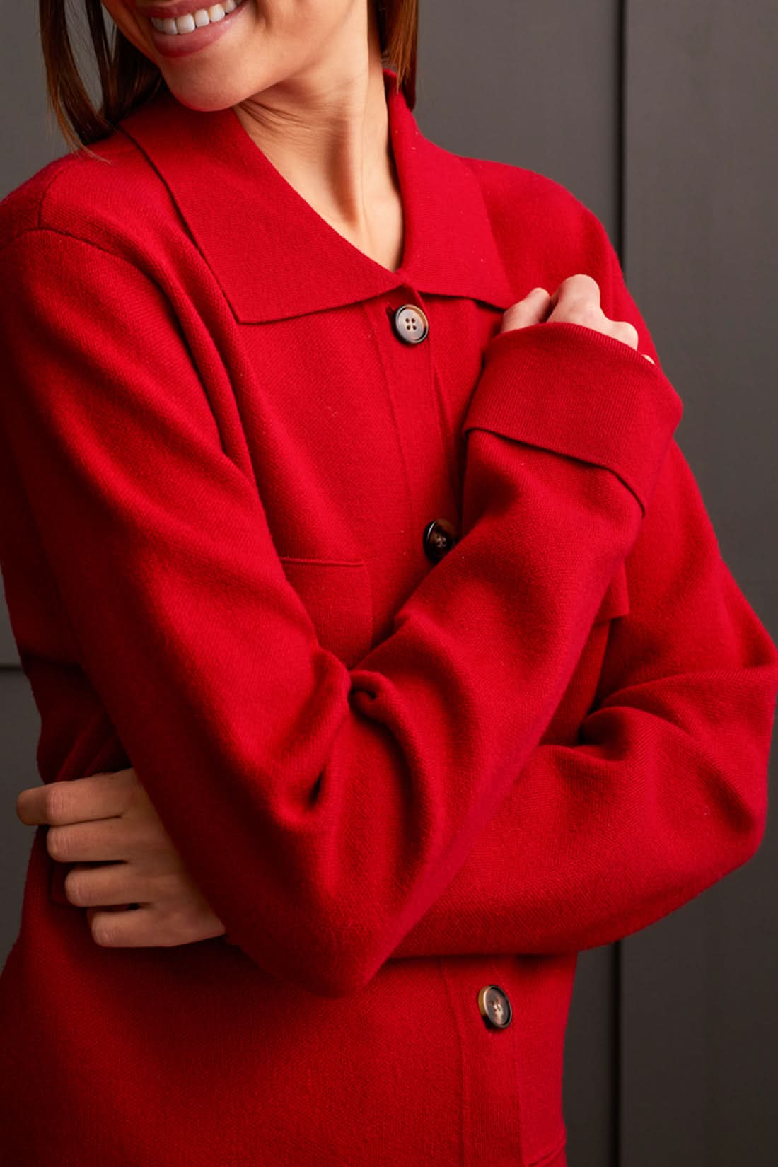 A person wearing the Tribal Sweater Cardigan with Collar and light-colored pants, standing against a dark paneled background, evokes the cozy allure of ultimate comfort.