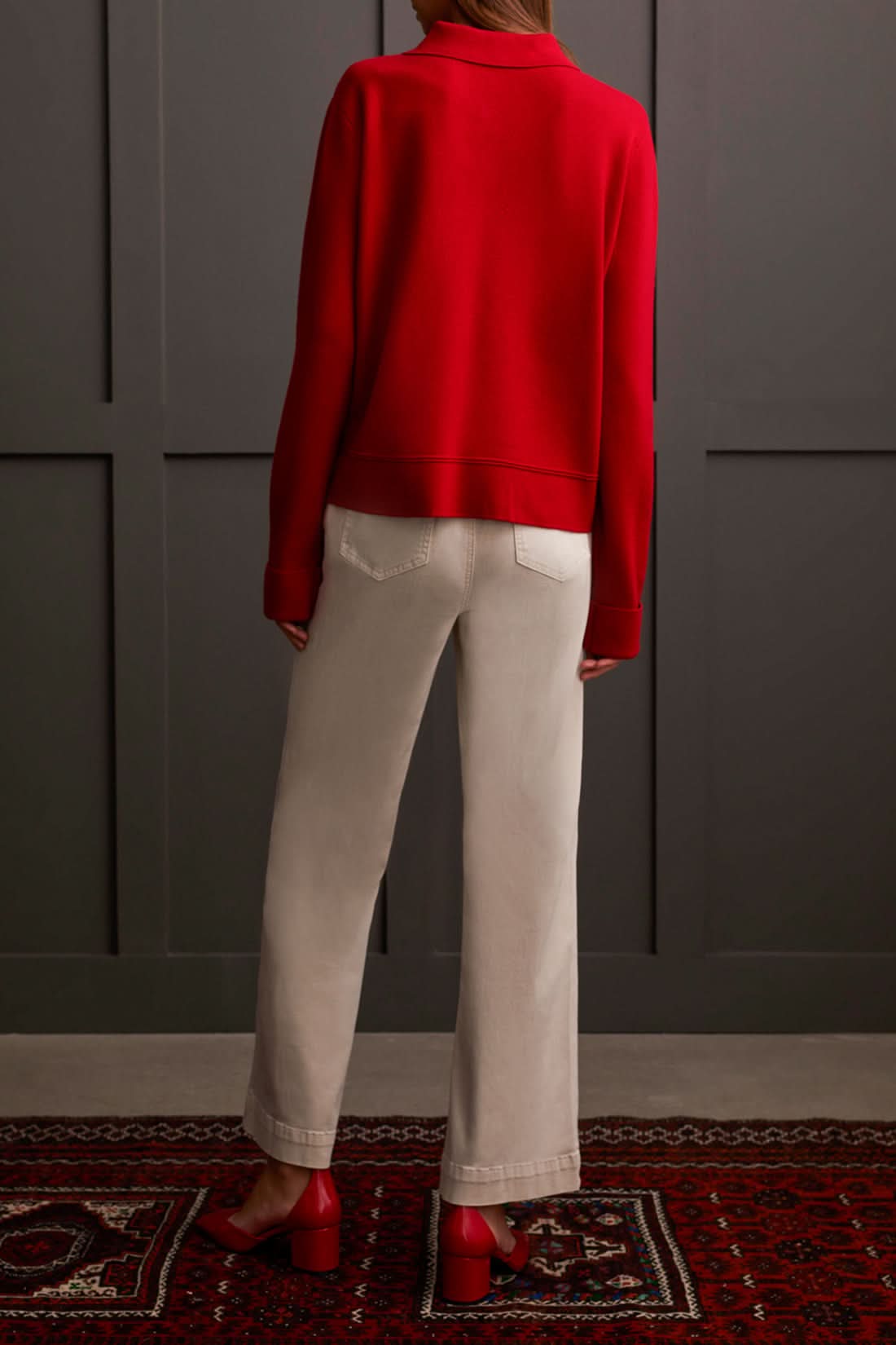 A person wearing the Tribal Sweater Cardigan with Collar and light-colored pants, standing against a dark paneled background, evokes the cozy allure of ultimate comfort.