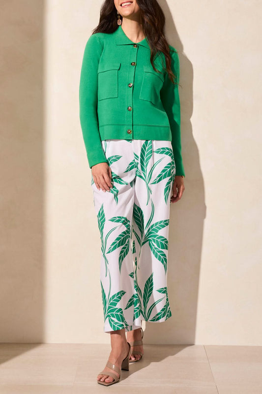 A person stands against a light wall wearing a Tribal DOUBLE KNIT COLLARED SWEATER CARDIGAN in green, accompanied by white and green leaf-patterned pants and beige sandals.