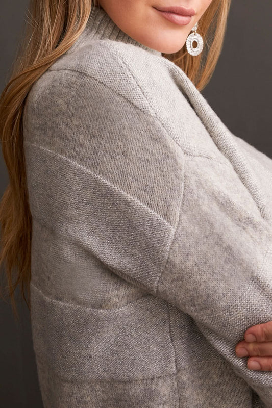 A person is modeling the Tribal Long Sleeve Mock Neck Sweater paired with black leather pants and heeled sandals, creating a chic look against a dark paneled wall—ideal for enhancing your fall wardrobe.