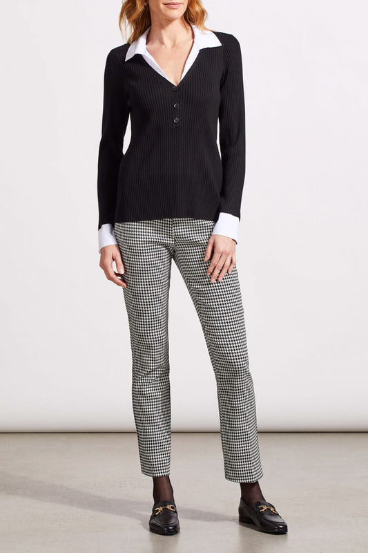 A person with shoulder-length hair is wearing a black ribbed cardigan with buttons over a white collared shirt, creating a fashionable look. The Tribal Henley Fooler Sweater adds an extra touch of sophistication, crafted from high-quality materials for enduring style.