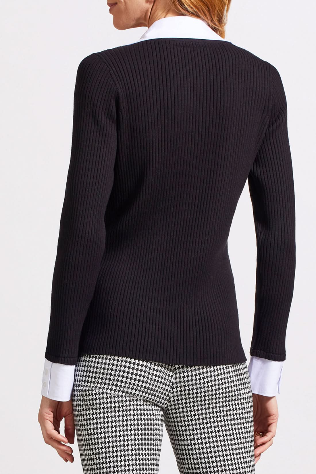 A person with shoulder-length hair is wearing a black ribbed cardigan with buttons over a white collared shirt, creating a fashionable look. The Tribal Henley Fooler Sweater adds an extra touch of sophistication, crafted from high-quality materials for enduring style.