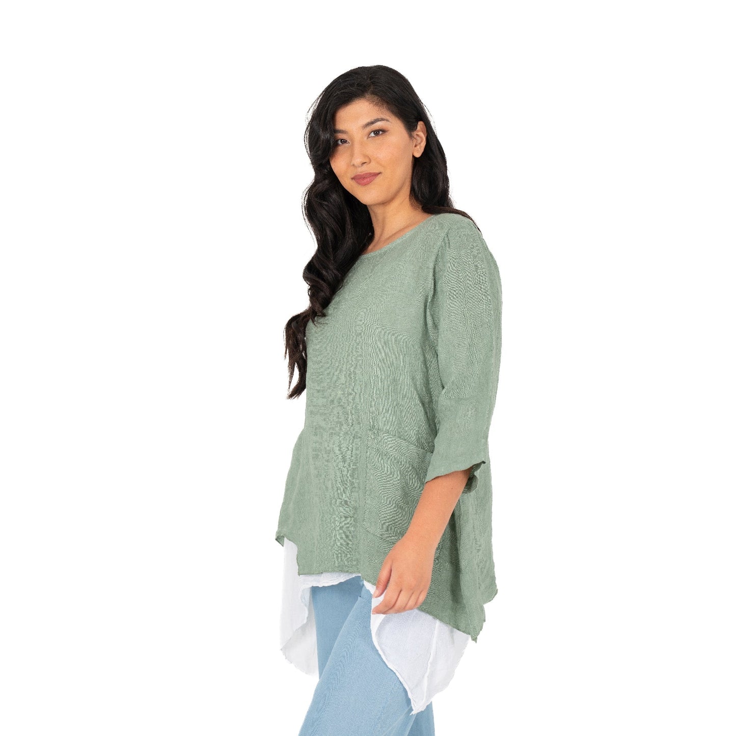 A person with long dark hair stands against a white background wearing the Layered Linen Tunic by M Made In Italy, paired with light blue pants and a white undershirt.