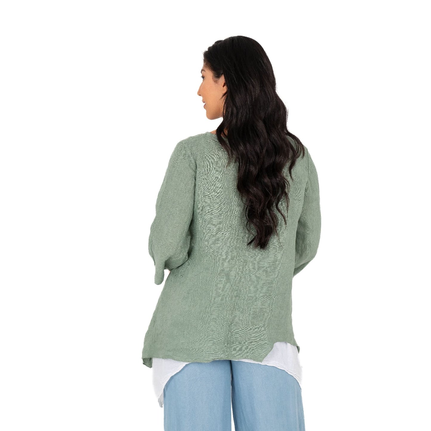 A person with long dark hair stands against a white background wearing the Layered Linen Tunic by M Made In Italy, paired with light blue pants and a white undershirt.
