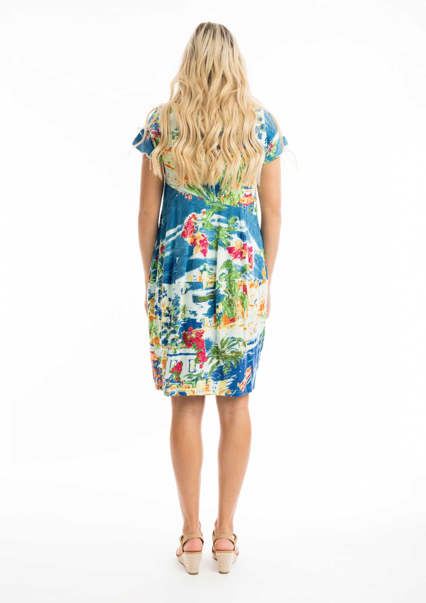 A woman wears the Orientique Easy Fit Short Summer Dress with a vibrant multicolored pattern, a flattering v neckline, and beige heeled sandals against a white background.