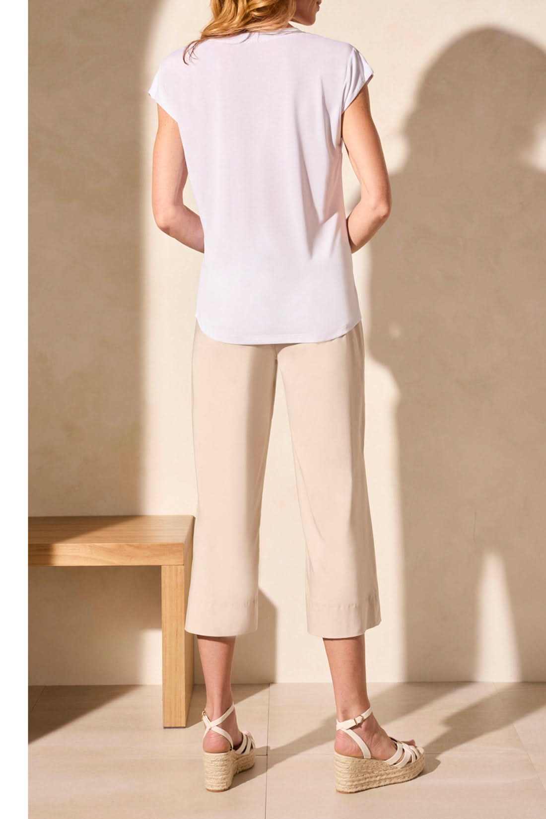 A person in a Tribal CAP SLEEVE V NECK TOP, beige wide-leg pants, and platform sandals stands against a light background, exuding timeless elegance.