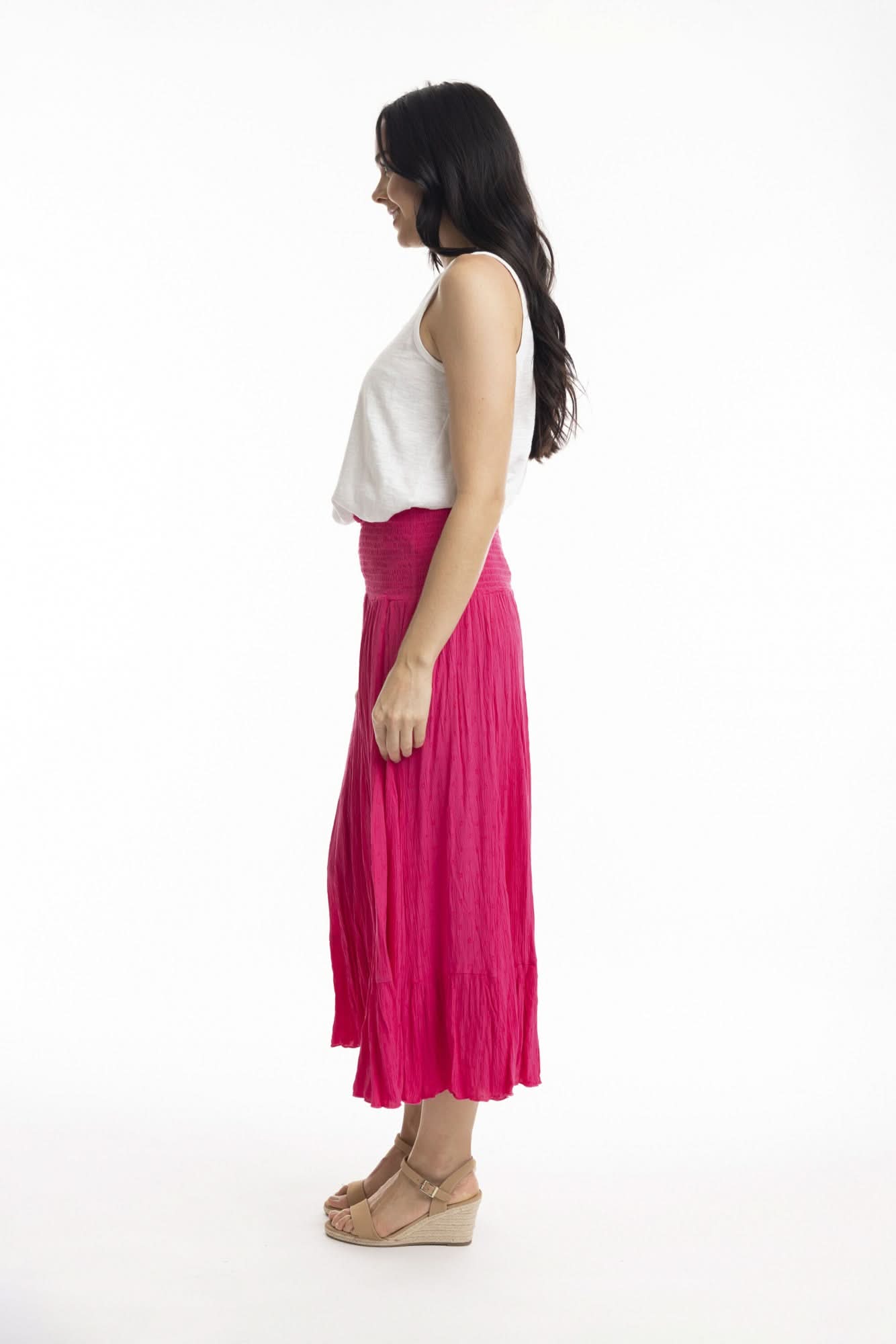 A woman stands against a white background wearing the Orientique Essentials Dobby Skirt Dress— a sleeveless, navy blue, knee-length style — paired with beige sandals and holding the sides of her dress.