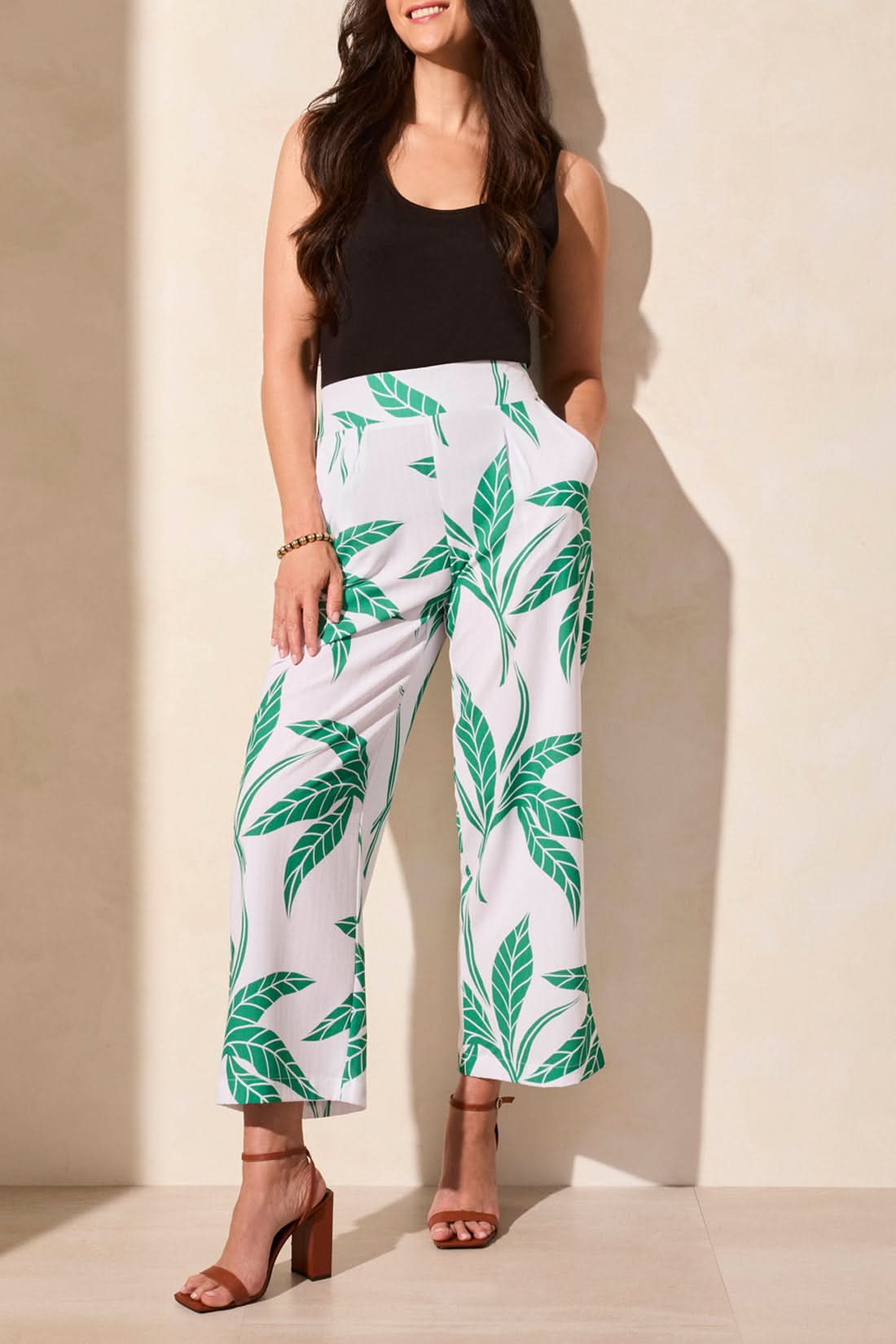 Against a neutral backdrop, an individual wears a navy top matched with Tribal's Pull On Ankle Pant with Pleats in a green-and-navy floral design. This stylish and versatile outfit blends functionality and effortless style, making it ideal for any occasion.