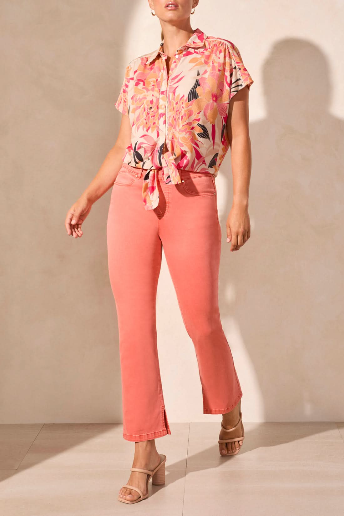 A person in a Tribal short sleeve top featuring buttons and a tie front, paired with coral pants and beige heeled sandals, stands on a light floor, exemplifying the ideal summer look.