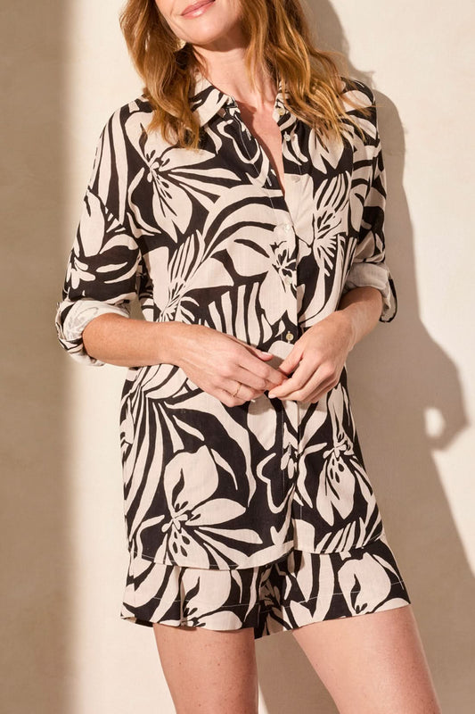 A woman wearing a Tribal black and white floral-patterned ROLL UP LONG SLEEVE BUTTON FRONT TOP stands against a light-colored wall with her arms partially crossed.