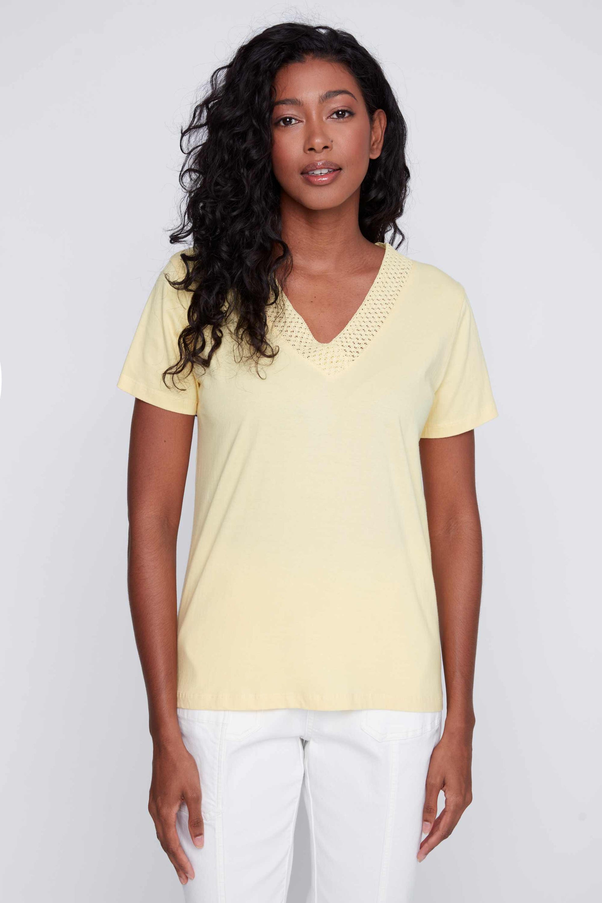 Woman in a white CoCo Y Club mesh detailed v-neck top and yellow pants posing against a gray background, exuding a fashion-forward vibe.