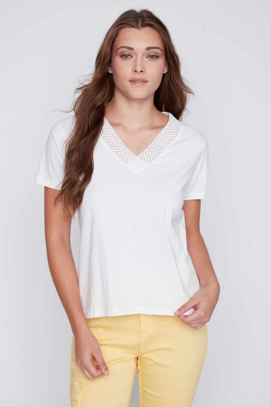 Woman in a white CoCo Y Club mesh detailed v-neck top and yellow pants posing against a gray background, exuding a fashion-forward vibe.