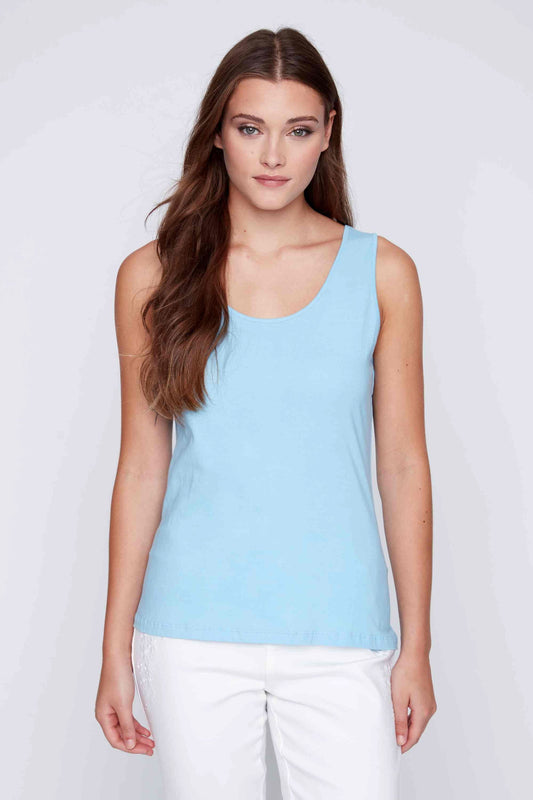 Woman posing in a CoCo Y Club versatile white Round Neck Tank and yellow pants against a grey background.