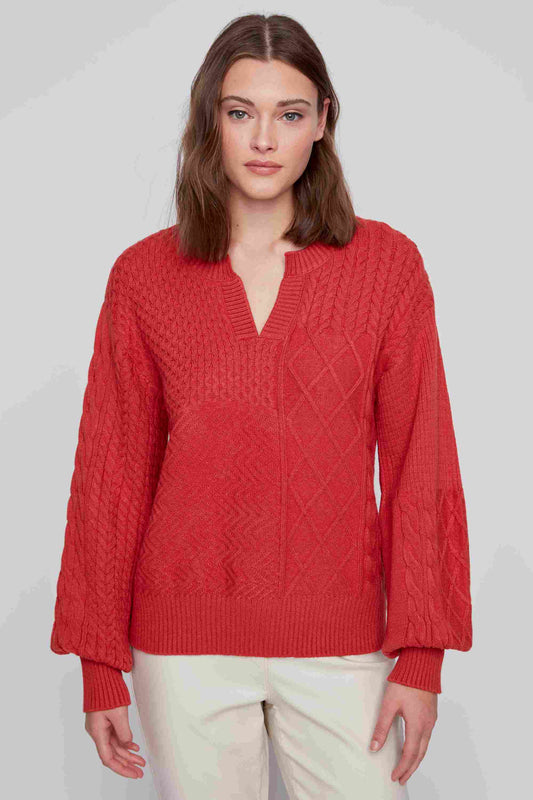 A person with short red hair, wearing a must-have piece from CoCo Y Club, a blue Textured V Neck Sweater, and maroon pants stands against a plain background, facing the camera.