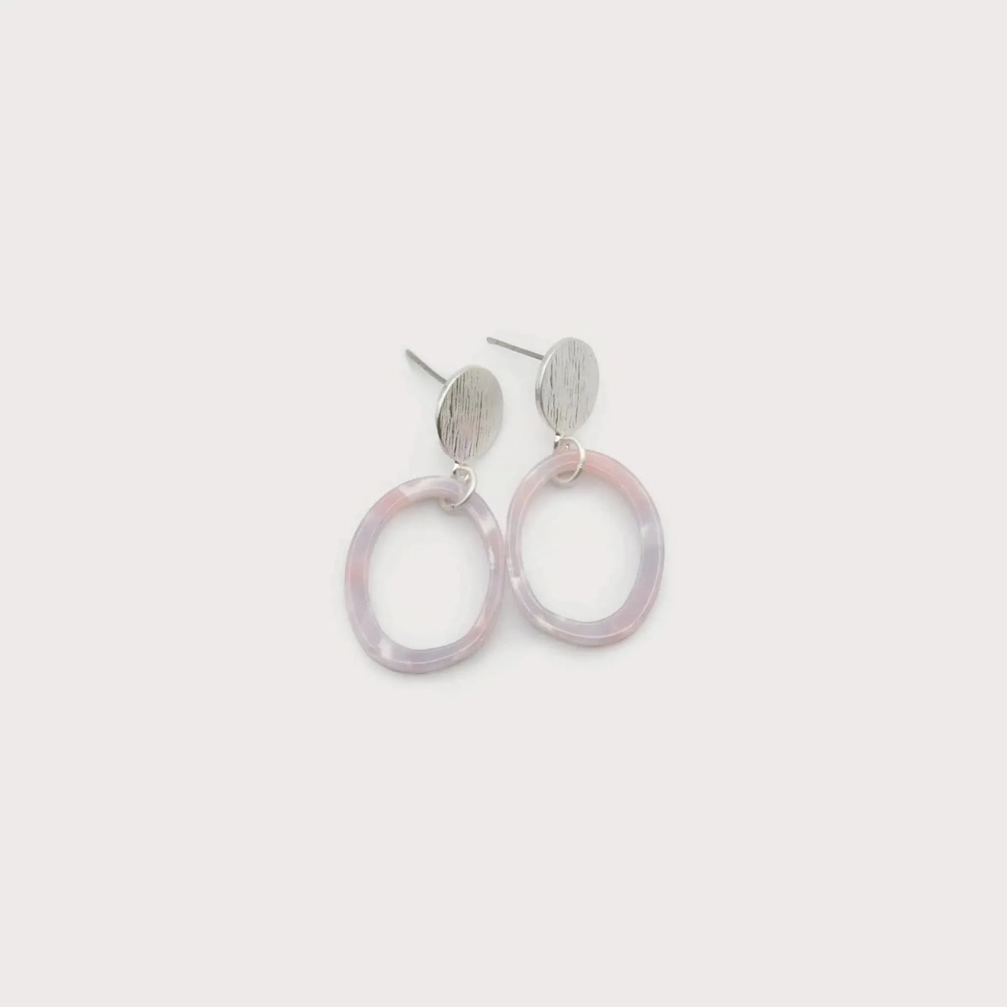 The Caracol Resin Hoop Earrings Passion Pink feature round, scratched metal studs paired with translucent pink resin hoops, shown on a plain white background.