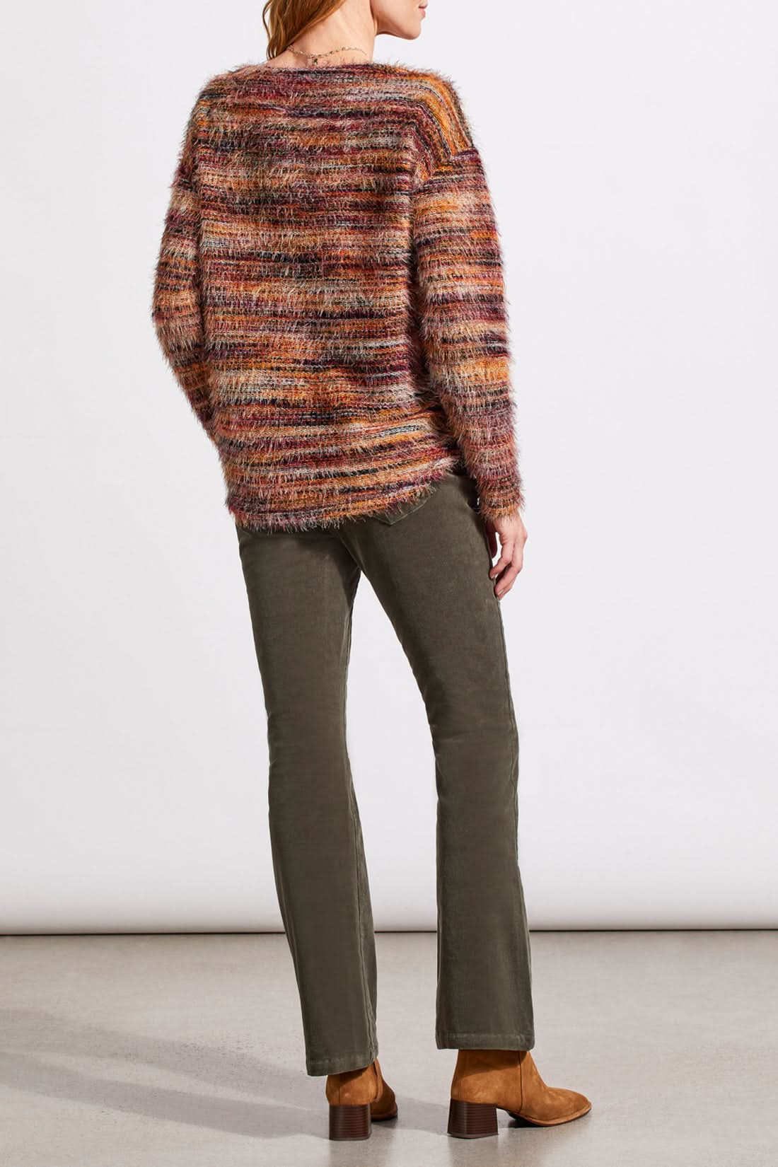 A person wearing a vibrant Tribal Soft Luxe Eyelash Long Sleeve Sweater in shades of orange, purple, and brown gently touches their hair.