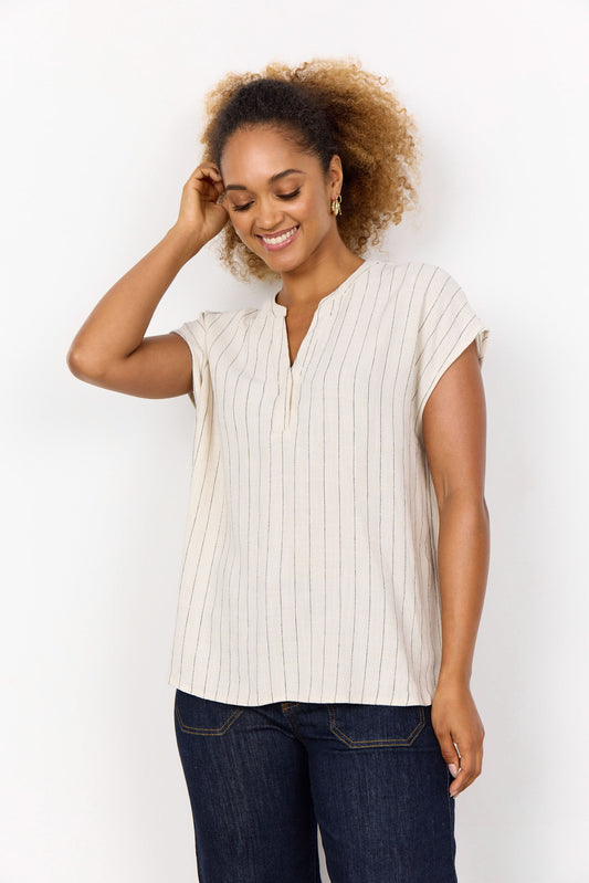A woman stands against a white background, smiling and touching her hair. She is wearing the Soya Concepts PAULA 1 Top, a light ECOVERO Viscose blouse with thin vertical stripes, paired with dark jeans.