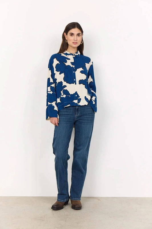 A woman wears the BLUE FLORAL PRINT BLOUSE by Soya Concepts, crafted from Ecovero viscose with bold blue abstract floral patterns, paired with blue jeans against a plain light background.